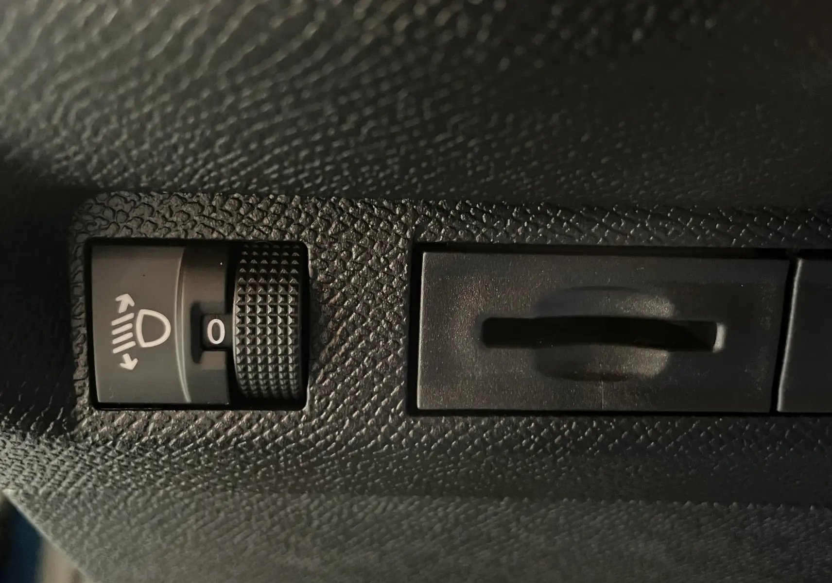 Gros plan sur le réglage de hauteur des phares dans l'habitacle d'une Peugeot 308 Hybrid 2025, surface noire texturée.