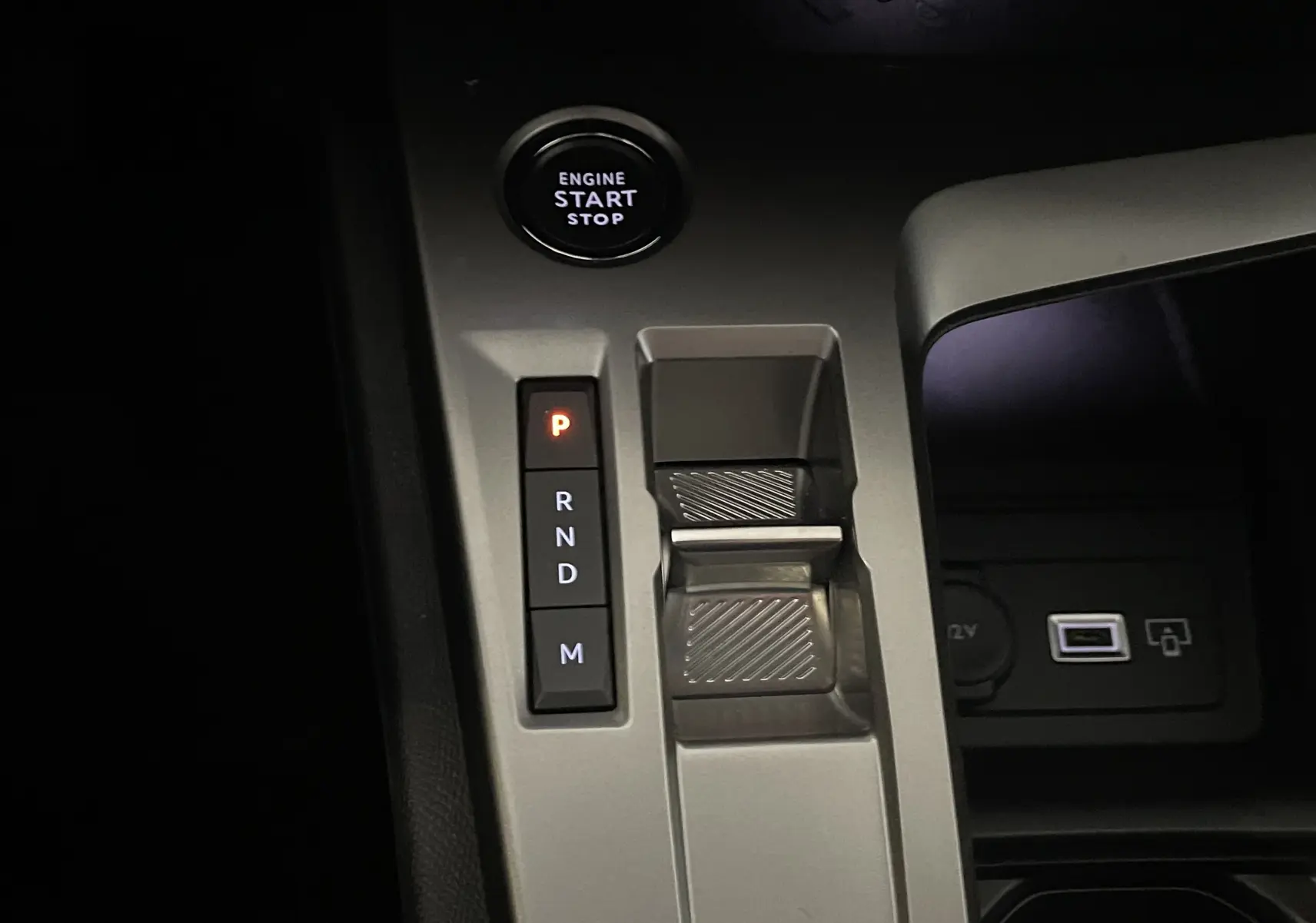 Gros plan sur la console centrale grise de la Peugeot 308 Hybrid 145, montrant le bouton start/stop et la commande de boîte automatique.