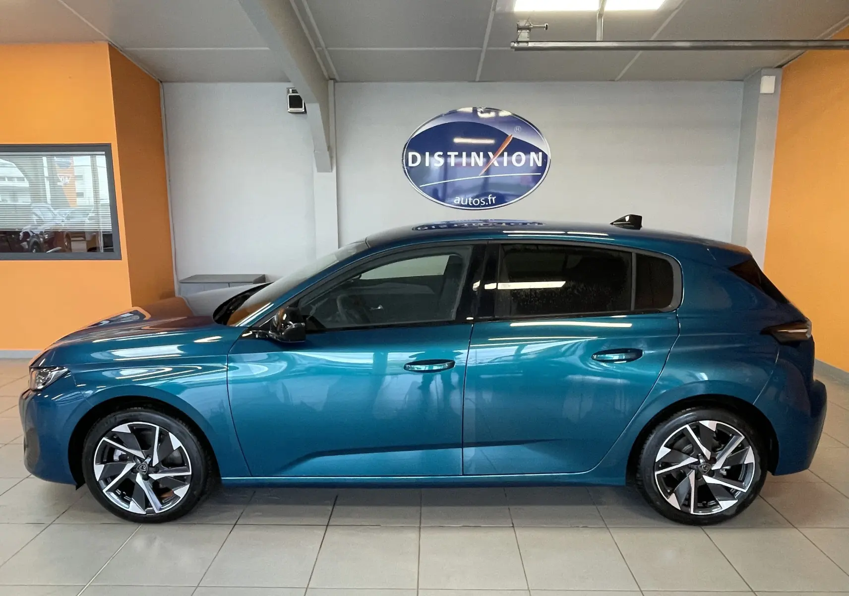 Profil latéral droit de la Peugeot 308 Hybrid 145 Allure en bleu obsession, avec jantes alliage 17 pouces dans un showroom.