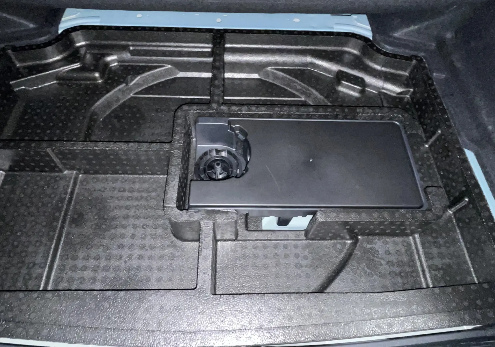 Vue rapprochée de l’espace de rangement sous le plancher de coffre d’une Peugeot 308 Hybrid 145 bleu obsession.