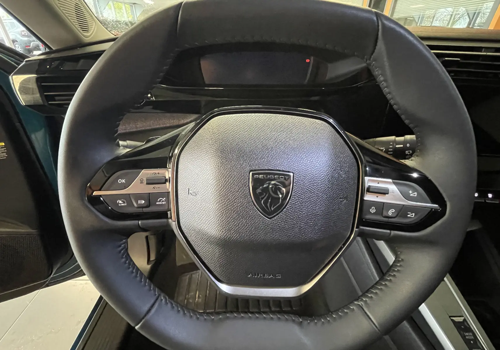 Vue rapprochée du volant cuir noir de la Peugeot 308 Hybrid 145 e-DCS6 Allure, avec commandes intégrées et logo lion central.