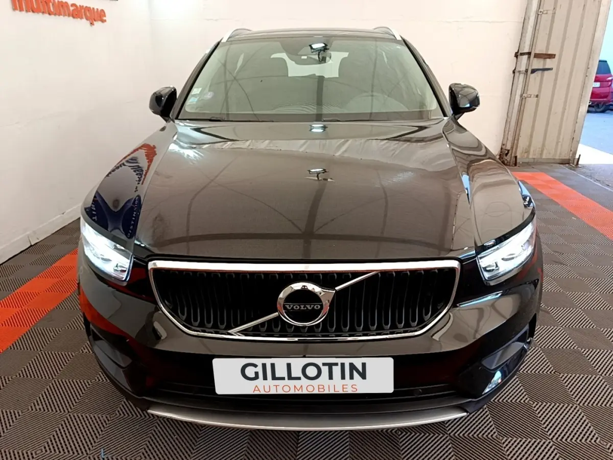 Vue avant d’un Volvo XC40 T2 noir avec calandre chromée et phares LED allumés dans un showroom.