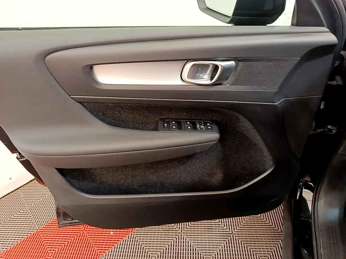 Vue intérieure côté gauche de la porte avant noire du Volvo XC40 T2 Momentum avec commandes de vitres et poignée chromée.