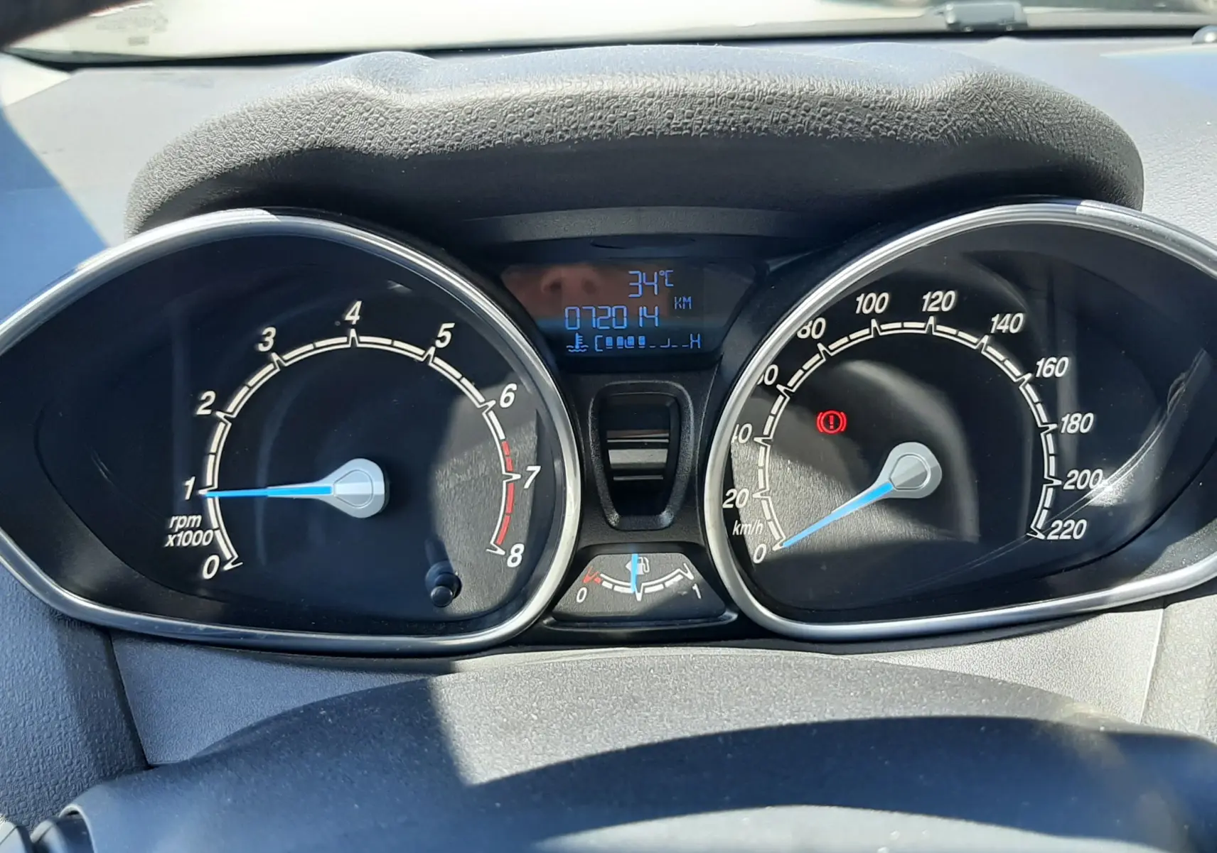Vue rapprochée du tableau de bord noir de la Ford Fiesta marron, affichant compte-tours, vitesse et température extérieure à 34°C.