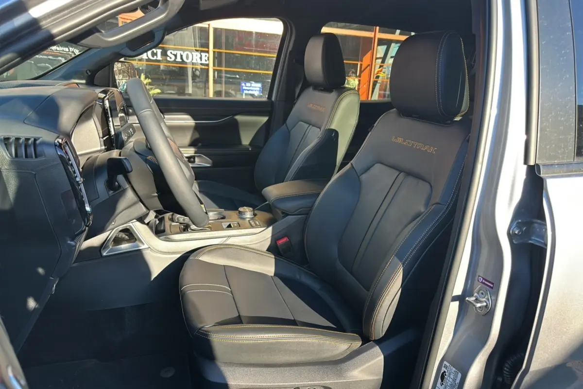 Vue intérieure côté conducteur du Ford Ranger 2025 gris iconic, sièges en cuir noirs avec surpiqûres jaunes et logo Wildtrak brodé.