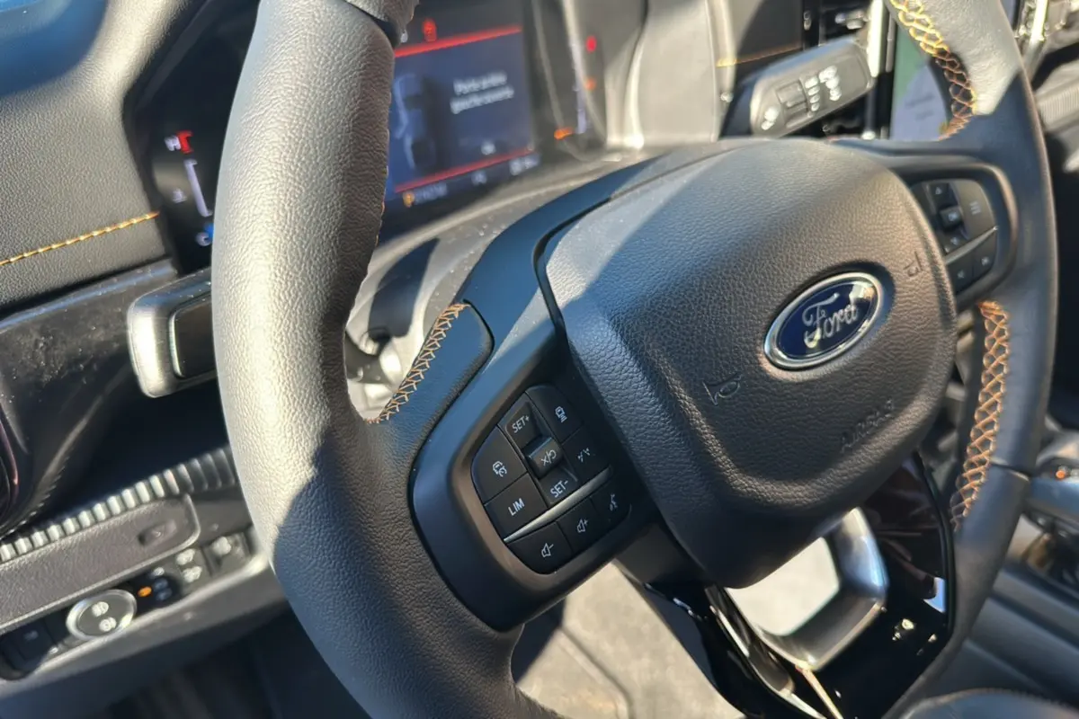 Gros plan sur le volant en cuir noir avec surpiqûres orange du Ford Ranger 2025, tableau de bord numérique en arrière-plan.