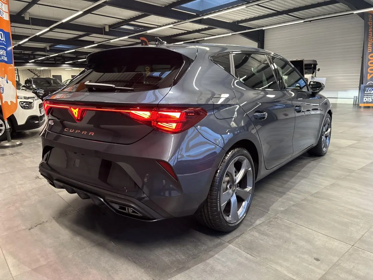 Vue 3/4 arrière droite d'une CUPRA Leon gris magnetic avec feux arrière Tri-LED et double sortie d'échappement noire.