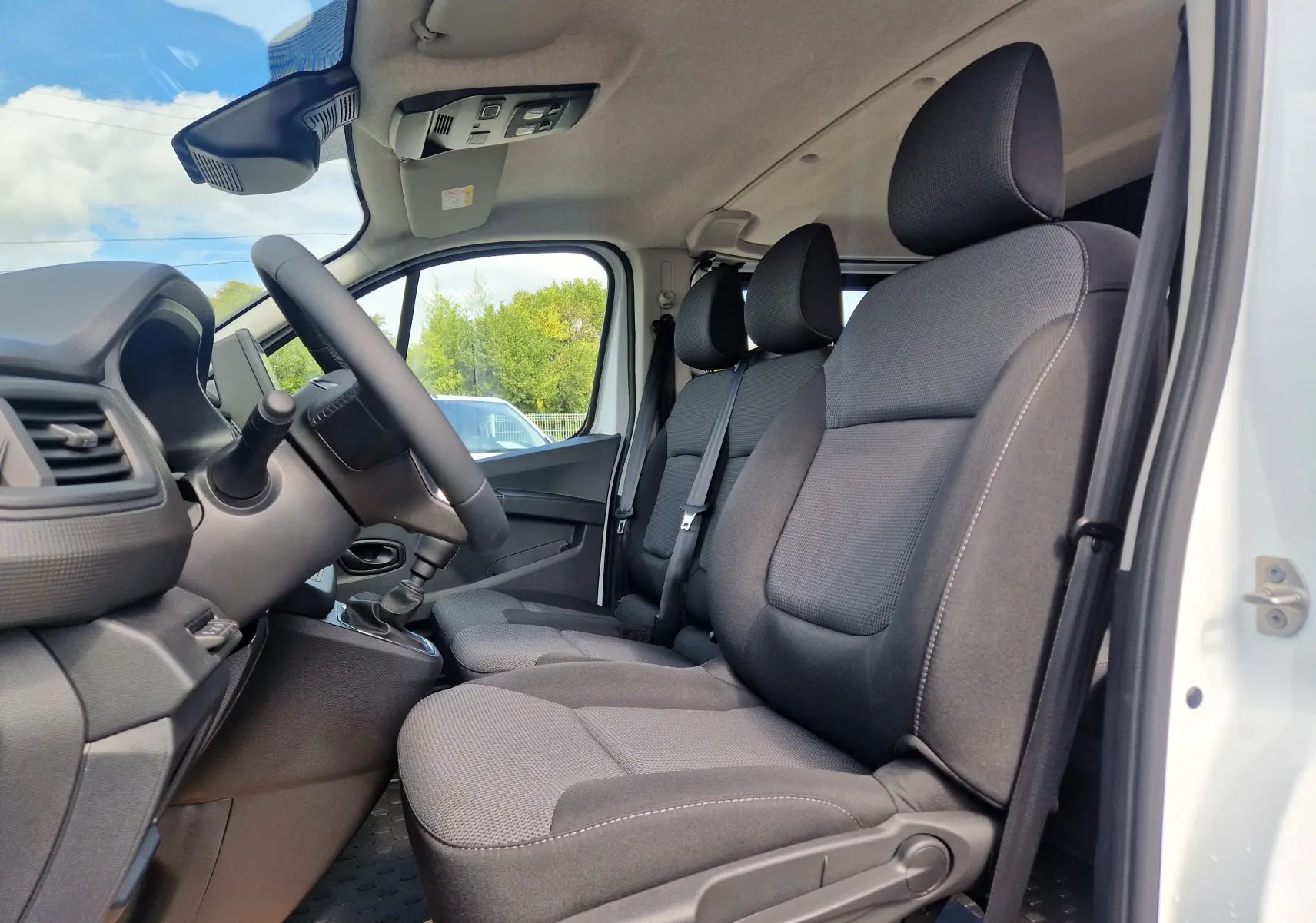 Vue intérieure côté conducteur du Renault Trafic blanc 2026, montrant les sièges avant noirs et le volant.