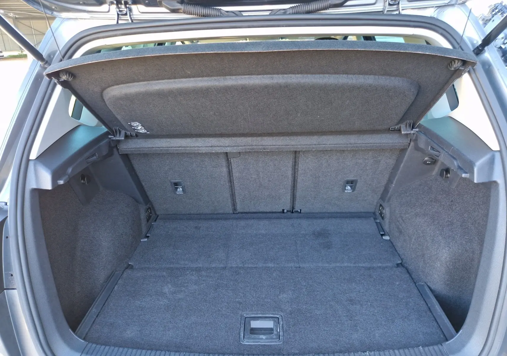 Coffre ouvert vu de l'arrière d'une Volkswagen Golf Sportsvan gris Indium Metal, montrant un espace de chargement spacieux et propre.