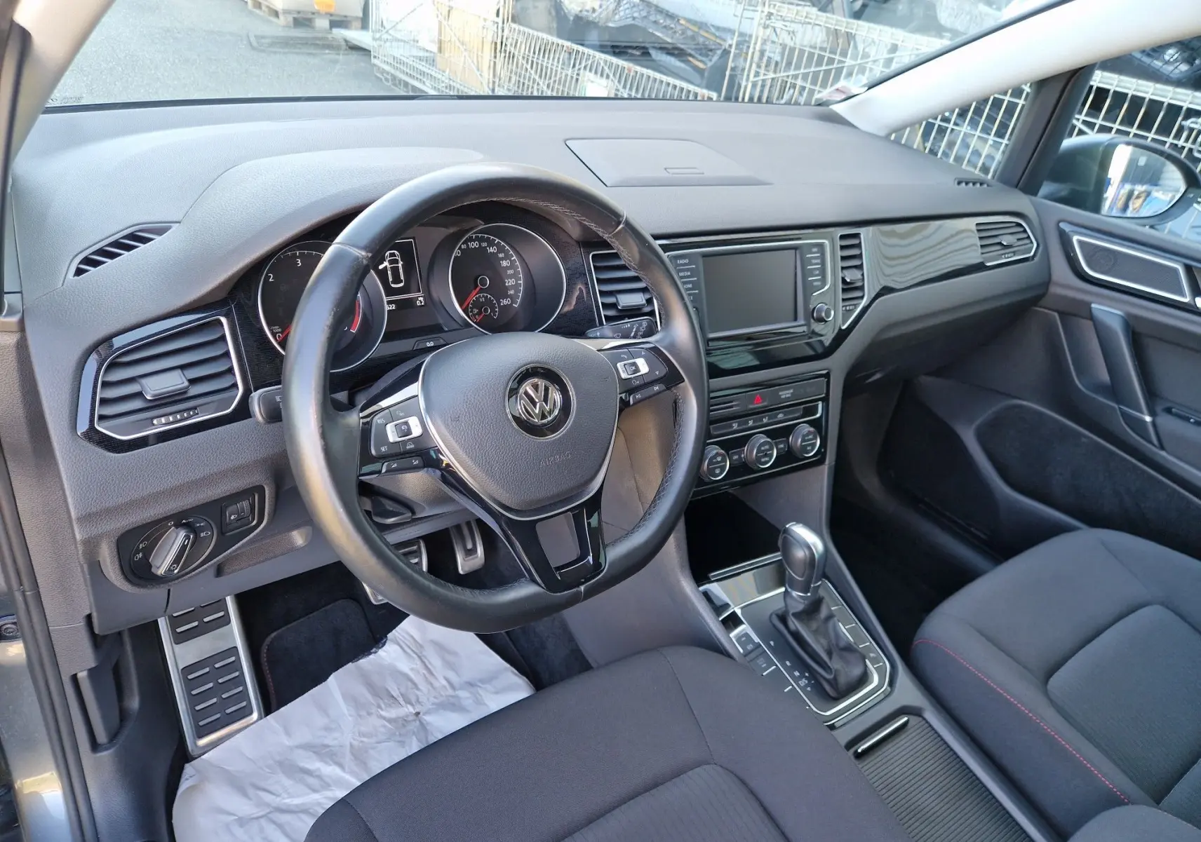 Vue intérieure côté conducteur de la Volkswagen Golf Sportsvan 2017, tableau de bord noir avec volant multifonction et levier de boîte automatique.