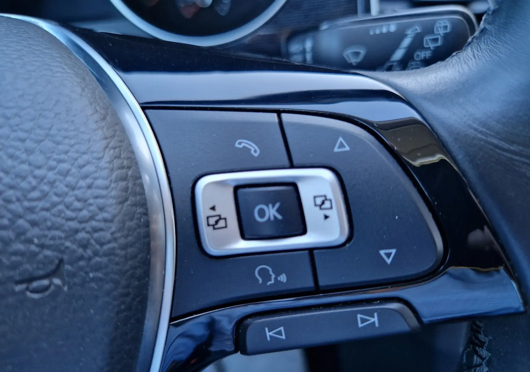 Gros plan sur les commandes multifonctions noires du volant en cuir d’une Volkswagen Golf Sportsvan gris Indium.