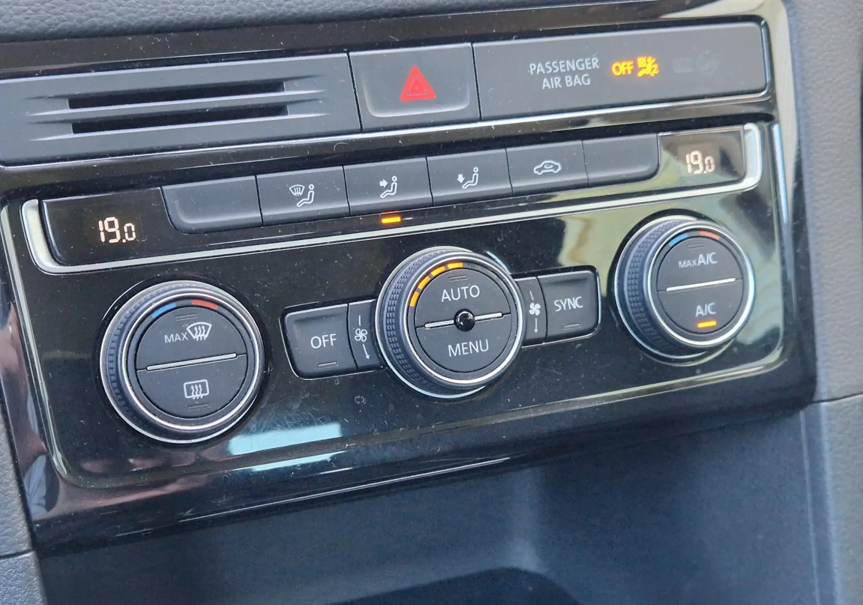 Gros plan sur la console de climatisation noire brillante du Volkswagen Golf Sportsvan gris Indium, avec affichage digital et boutons ronds.