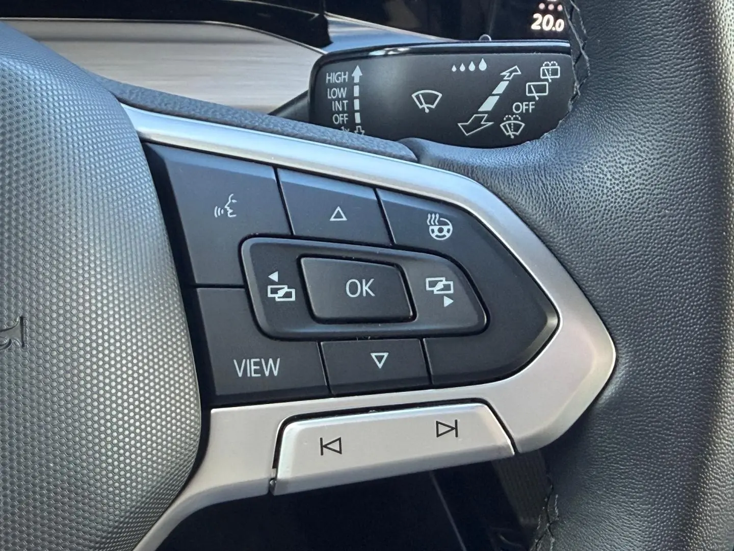 Gros plan sur les commandes multifonctions noires et argent du volant cuir de la Volkswagen Golf gris lunaire 2024.