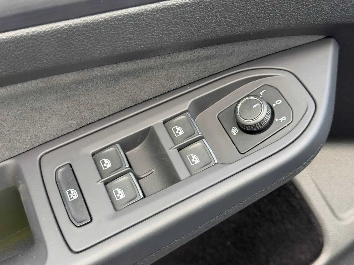 Gros plan sur les commandes de lève-vitres et réglage des rétroviseurs côté conducteur de la Volkswagen Golf gris lunaire 2024.