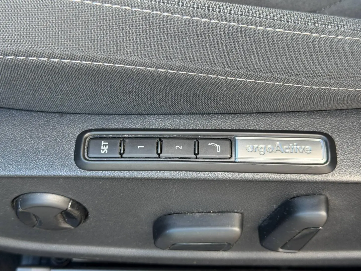 Gros plan sur les commandes de réglage mémoire ergoActive du siège avant côté conducteur, tissu gris.