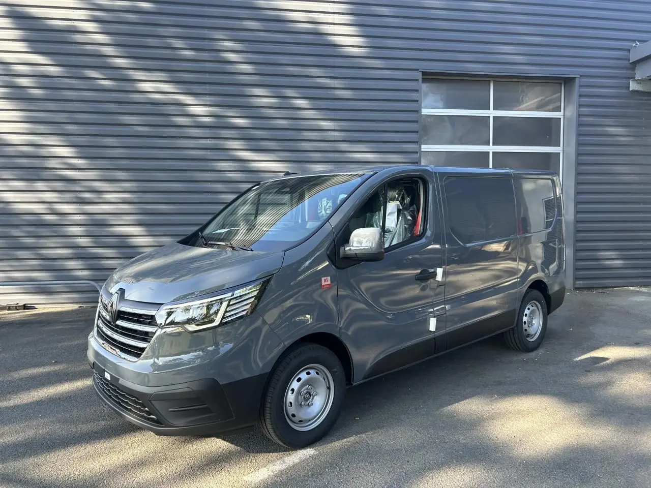 Renault Trafic Fourgon gris urbain vu en 3/4 avant droit, avec jantes acier et caméra de recul intégrée.