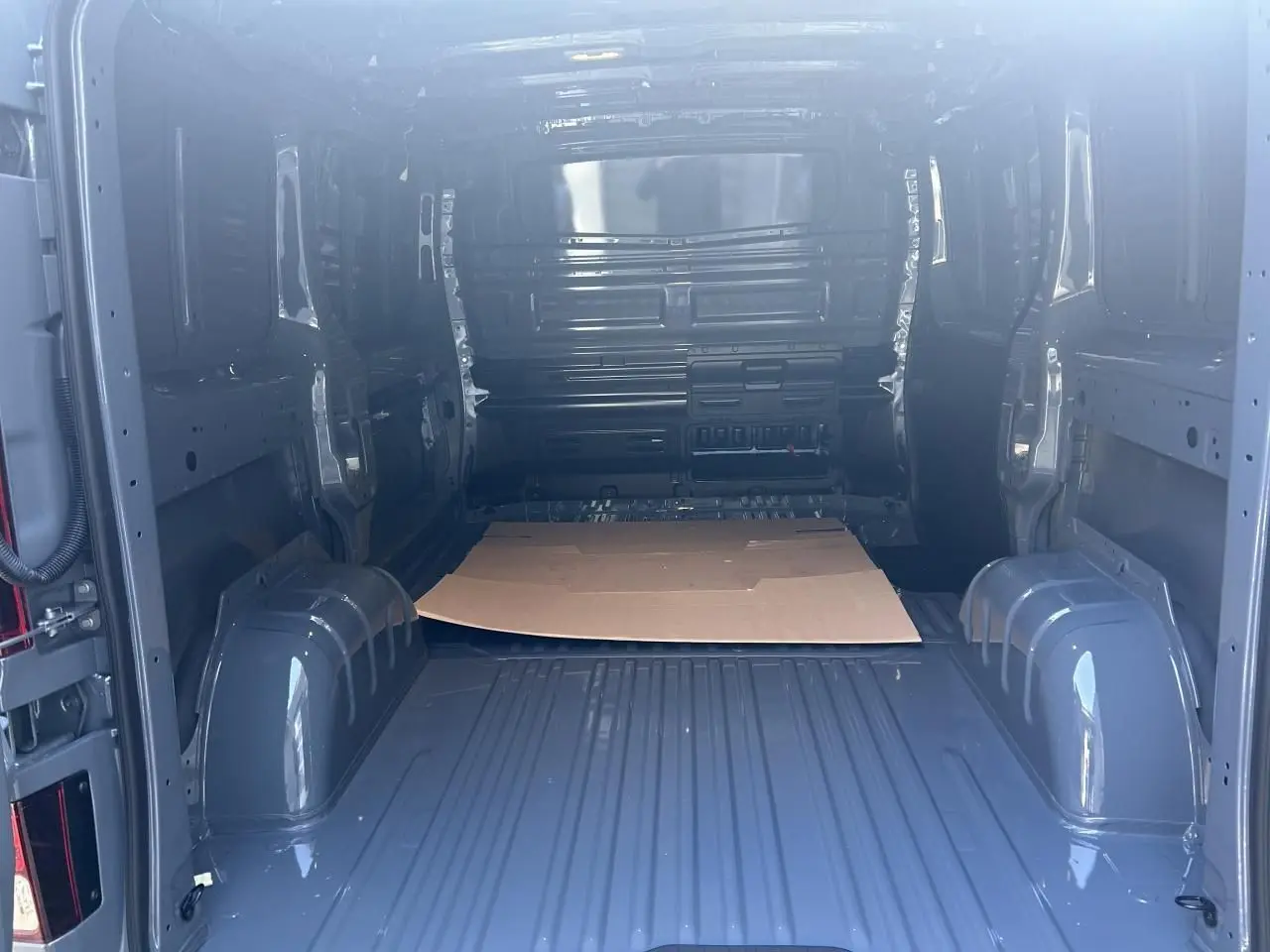 Intérieur du fourgon Renault Trafic L1H1 Gris Urbain vu de l'arrière, montrant l'espace de chargement vide et les passages de roues.