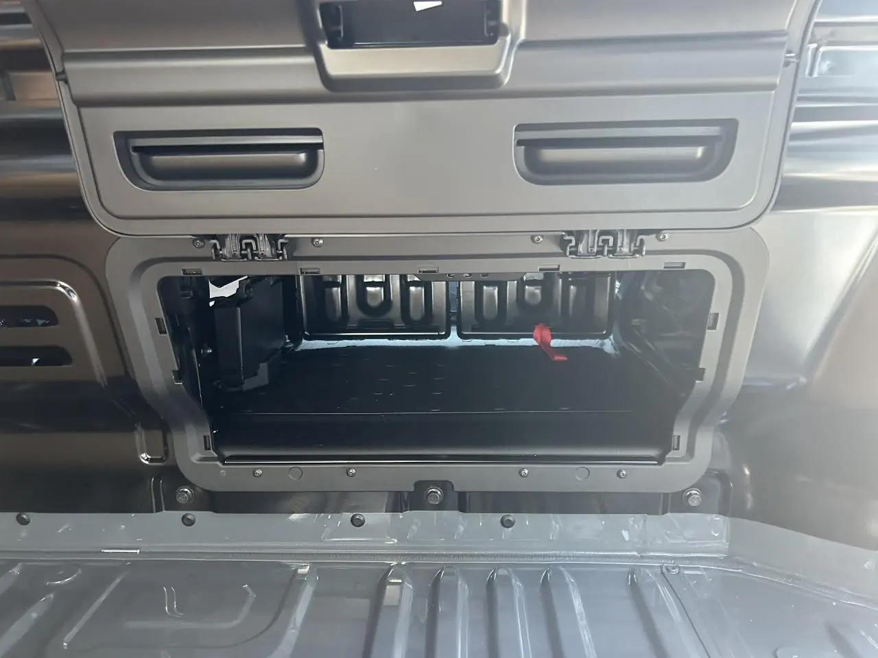 Gros plan sur la trappe de cloison ouverte du Renault Trafic Fourgon gris urbain, montrant l'espace de rangement intérieur.