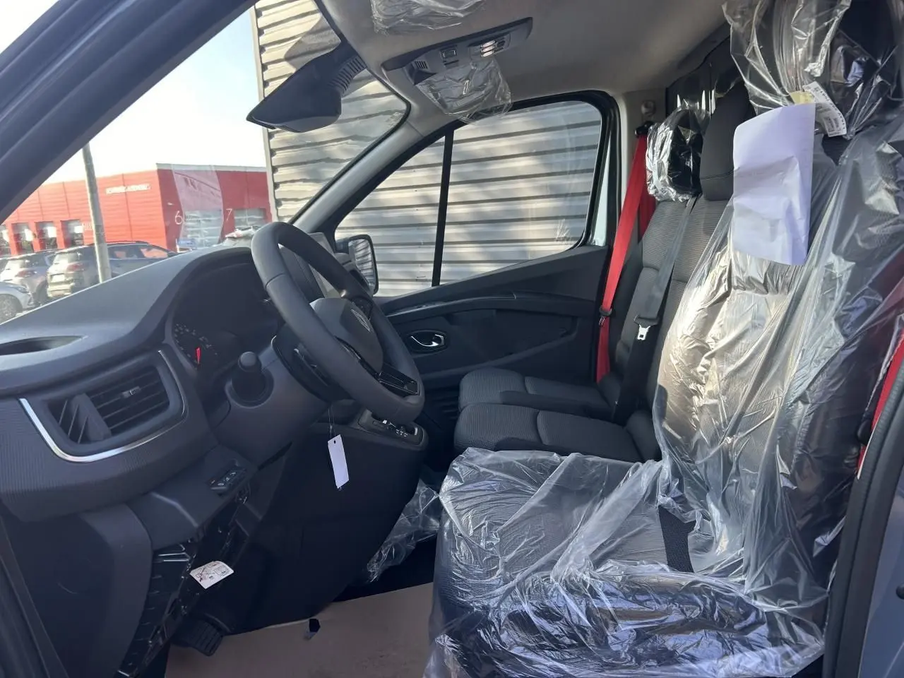 Intérieur du Renault Trafic Fourgon 2025 vu côté conducteur, sièges avant protégés par film plastique et ceinture rouge visible.