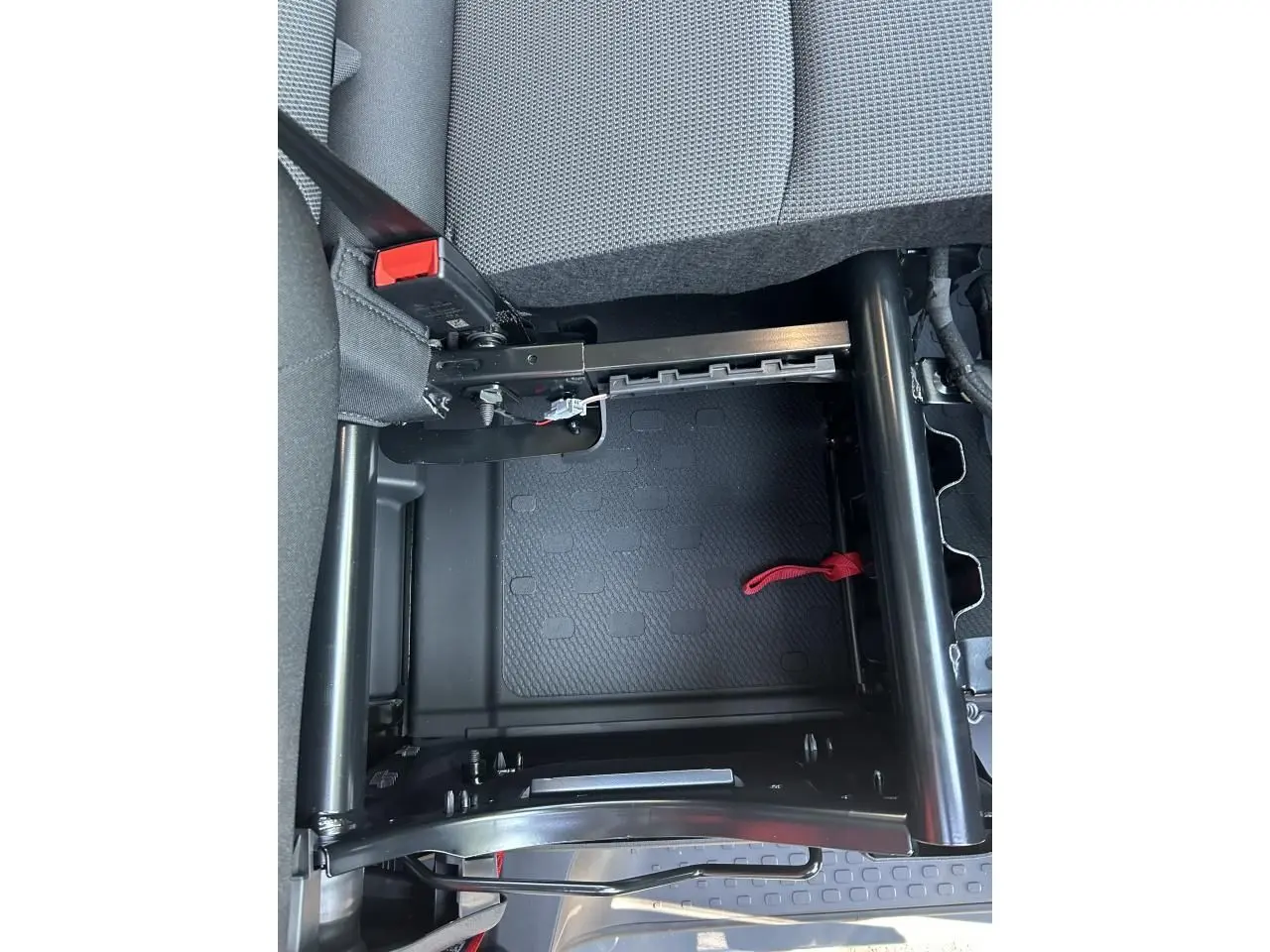 Gros plan sous la banquette rabattable du Renault Trafic Fourgon gris urbain, montrant la structure métallique et la sangle rouge.