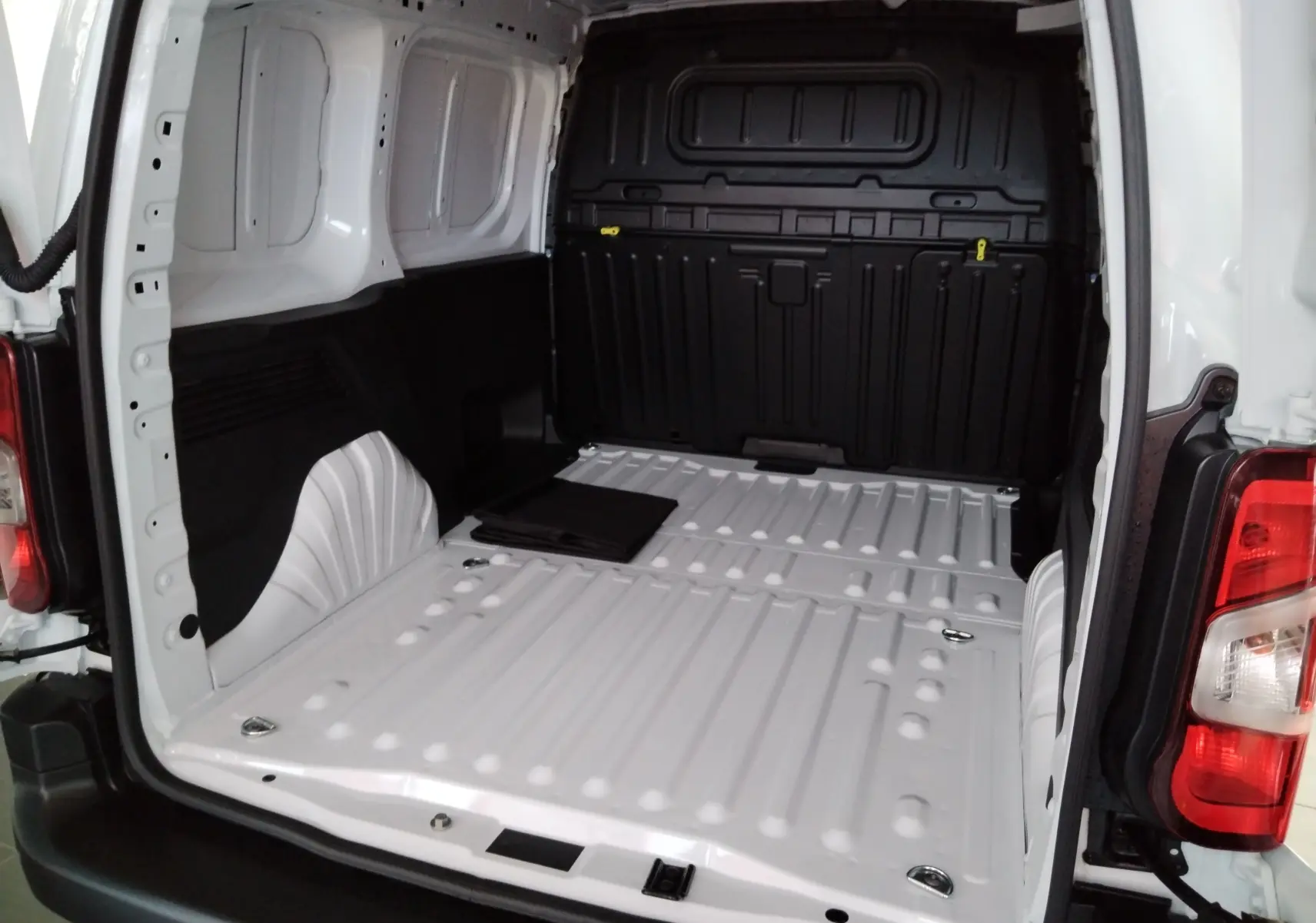 Vue intérieure arrière du coffre blanc Icy du Peugeot Partner FGN 2025, avec plancher métallique et anneaux d'arrimage visibles.