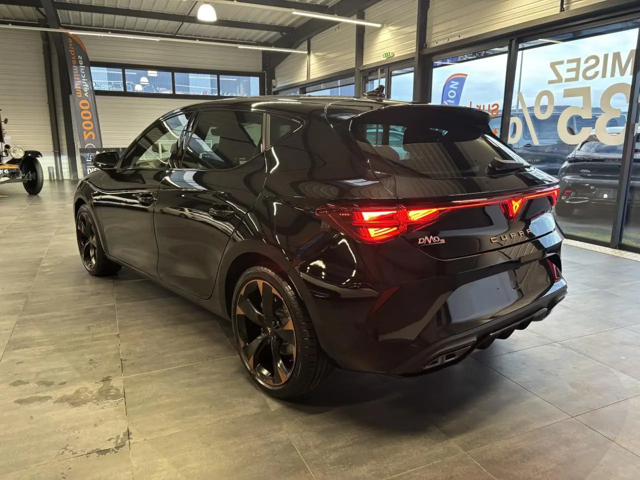 Vue 3/4 arrière droite d'une CUPRA Leon noir midnight avec feux arrière Tri-LED et jantes alliage 18'' cuivrées.