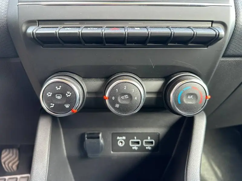 Gros plan sur les commandes de climatisation manuelle d'une Renault Clio gris 2023, avec boutons rotatifs et ports USB visibles.