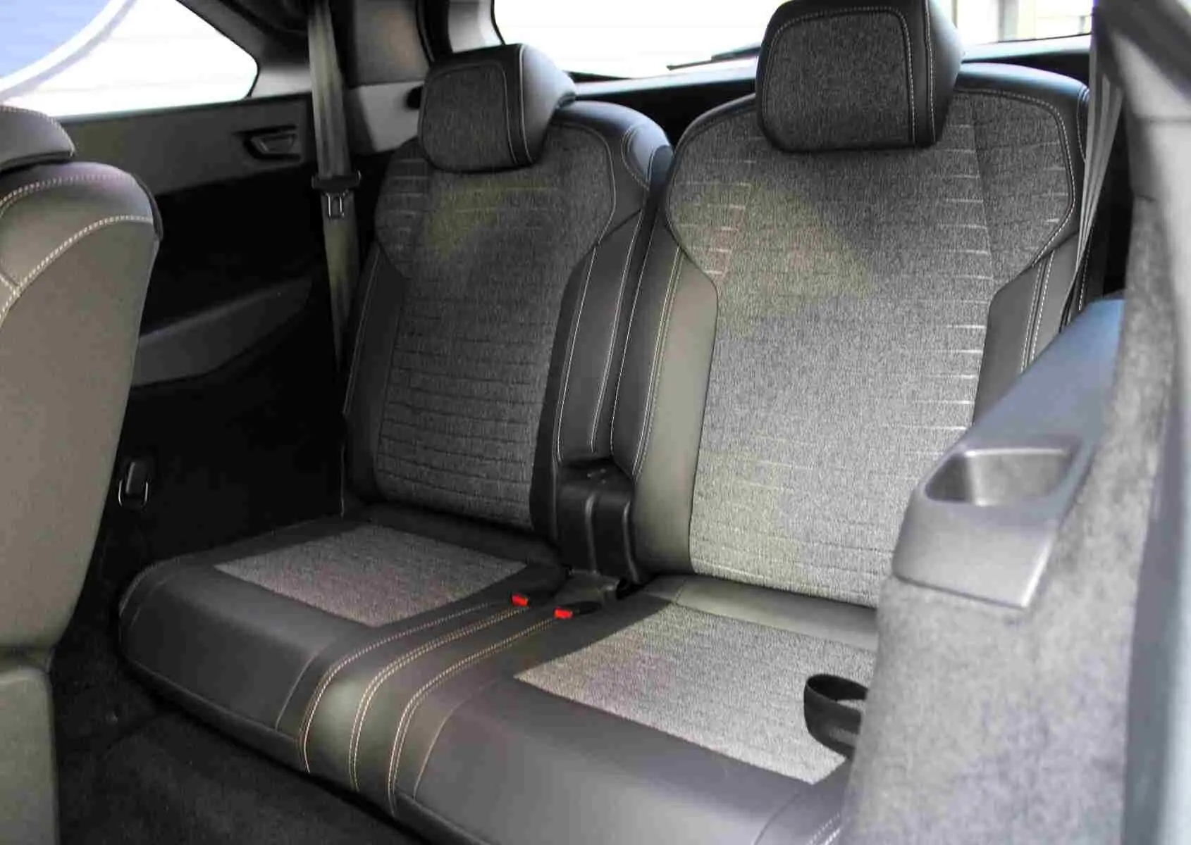 Vue intérieure arrière droite des sièges gris tissu et cuir du Peugeot 5008 Hybrid 2025, finition Allure avec surpiqûres contrastées.
