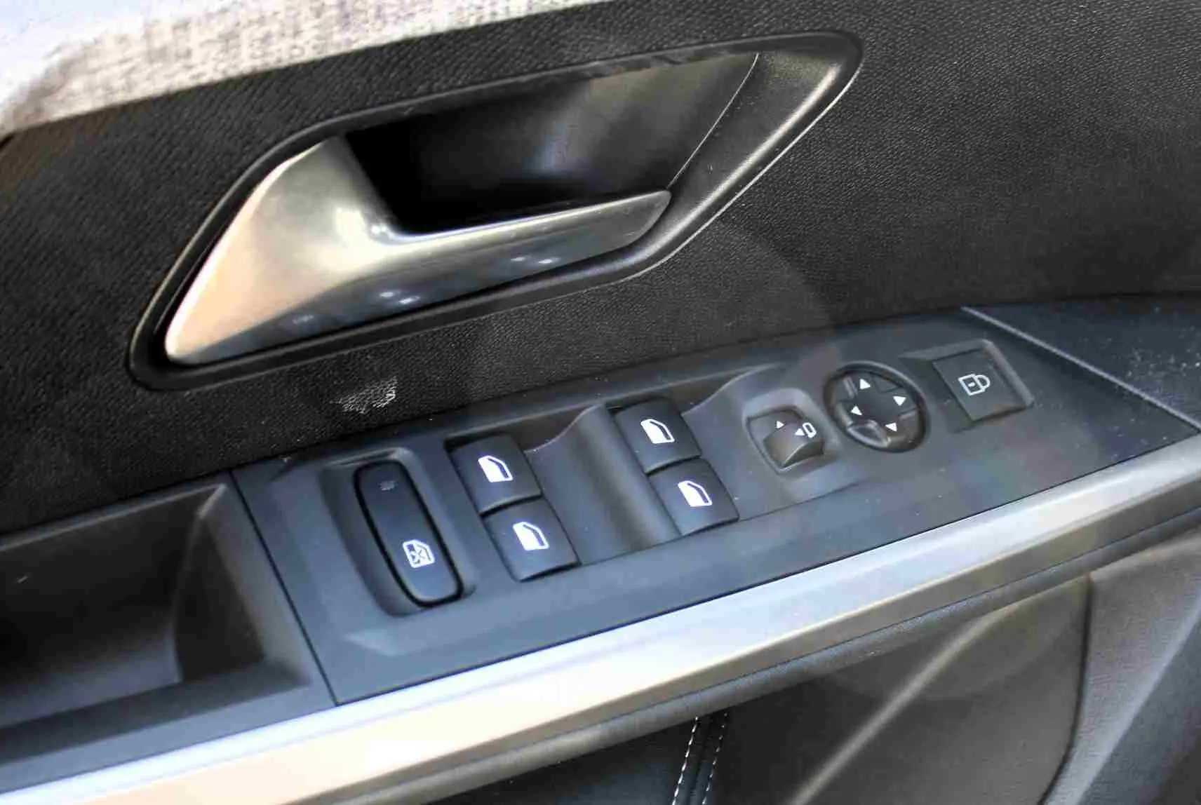 Gros plan sur la commande des vitres et la poignée intérieure côté gauche d’un Peugeot 5008 gris titane hybride.