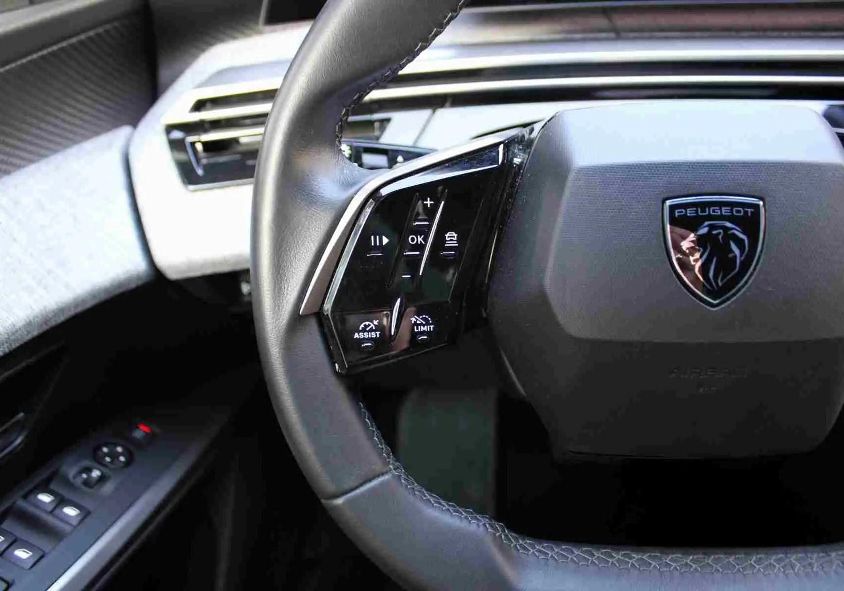 Gros plan sur le volant cuir noir du Peugeot 5008 2025 avec commandes intégrées et logo lion chromé central.