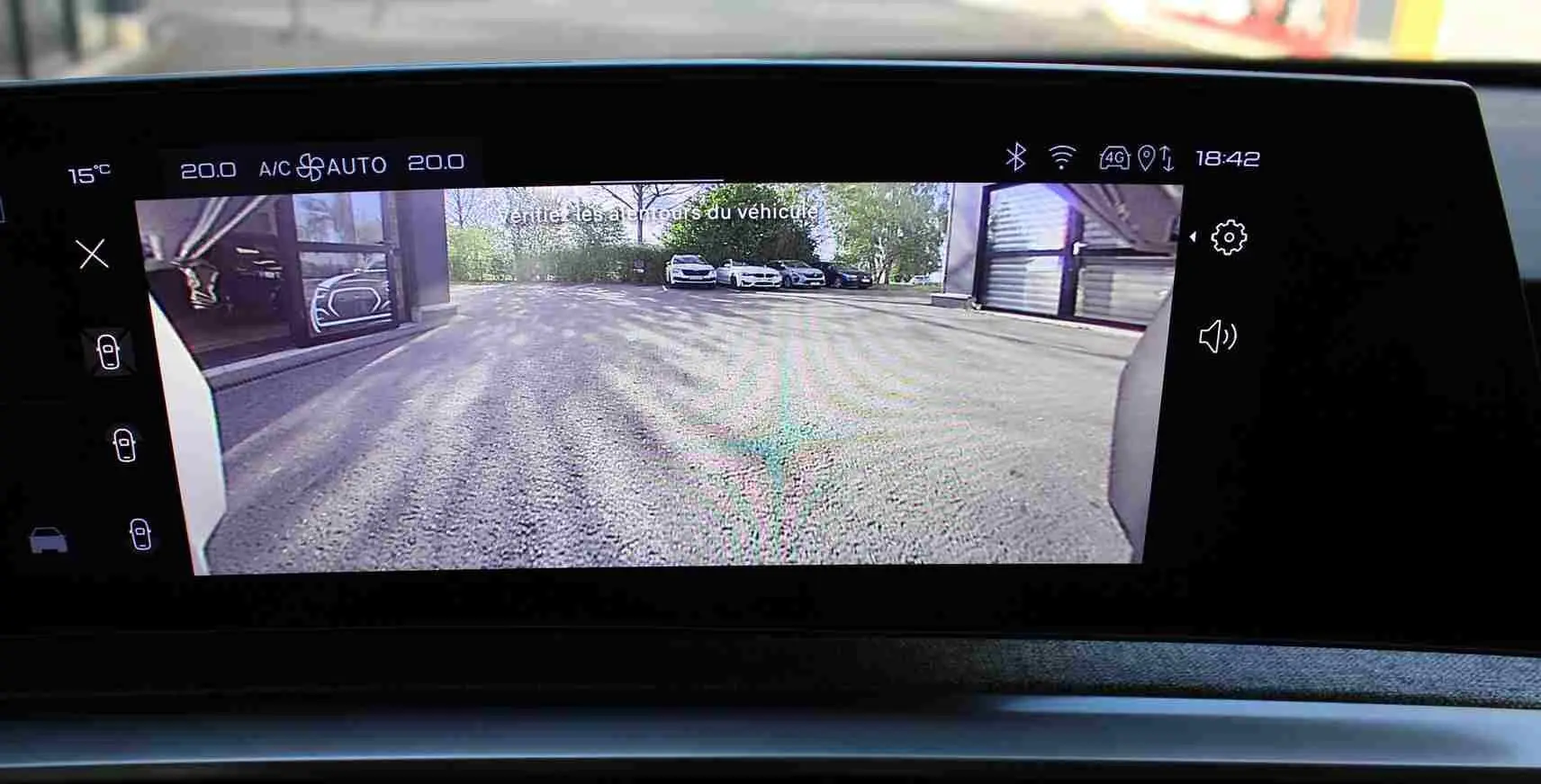Vue de l'écran intérieur du Peugeot 5008 Hybrid gris titane montrant la caméra de recul avec parking extérieur visible.