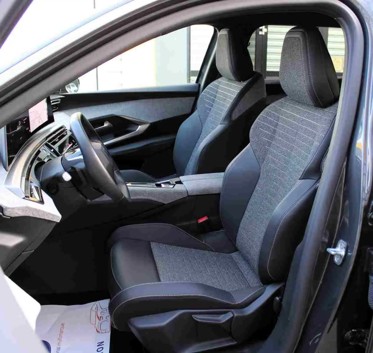 Vue intérieure côté conducteur du Peugeot 5008 gris titane, mettant en valeur les sièges bi-matière gris et noir avec surpiqûres contrastantes.