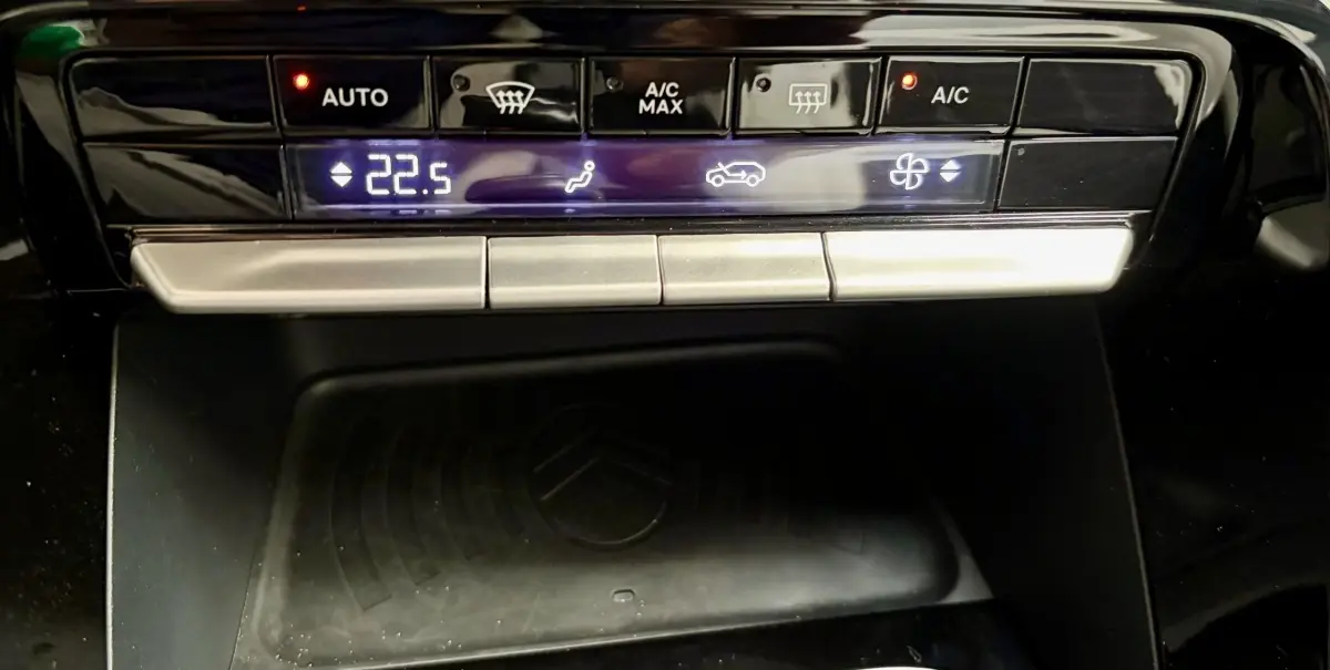 Gros plan sur la console centrale noire du Citroën C3 2025, montrant les commandes climatisation et zone de recharge induction.