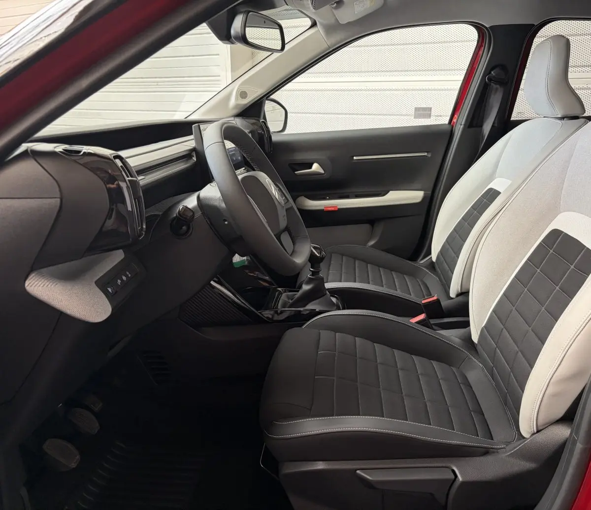 Vue intérieure côté conducteur de la Citroën C3 2025, sièges bicolores noirs et gris avec volant cuir multifonctions.