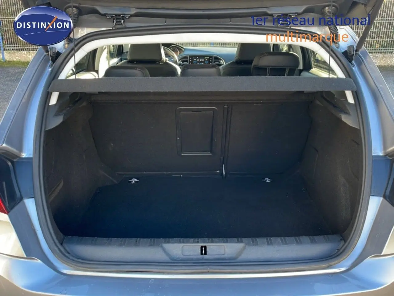 Coffre ouvert d’une Peugeot 308 gris Artense métal, vue arrière montrant l’espace de chargement vide et la banquette arrière.