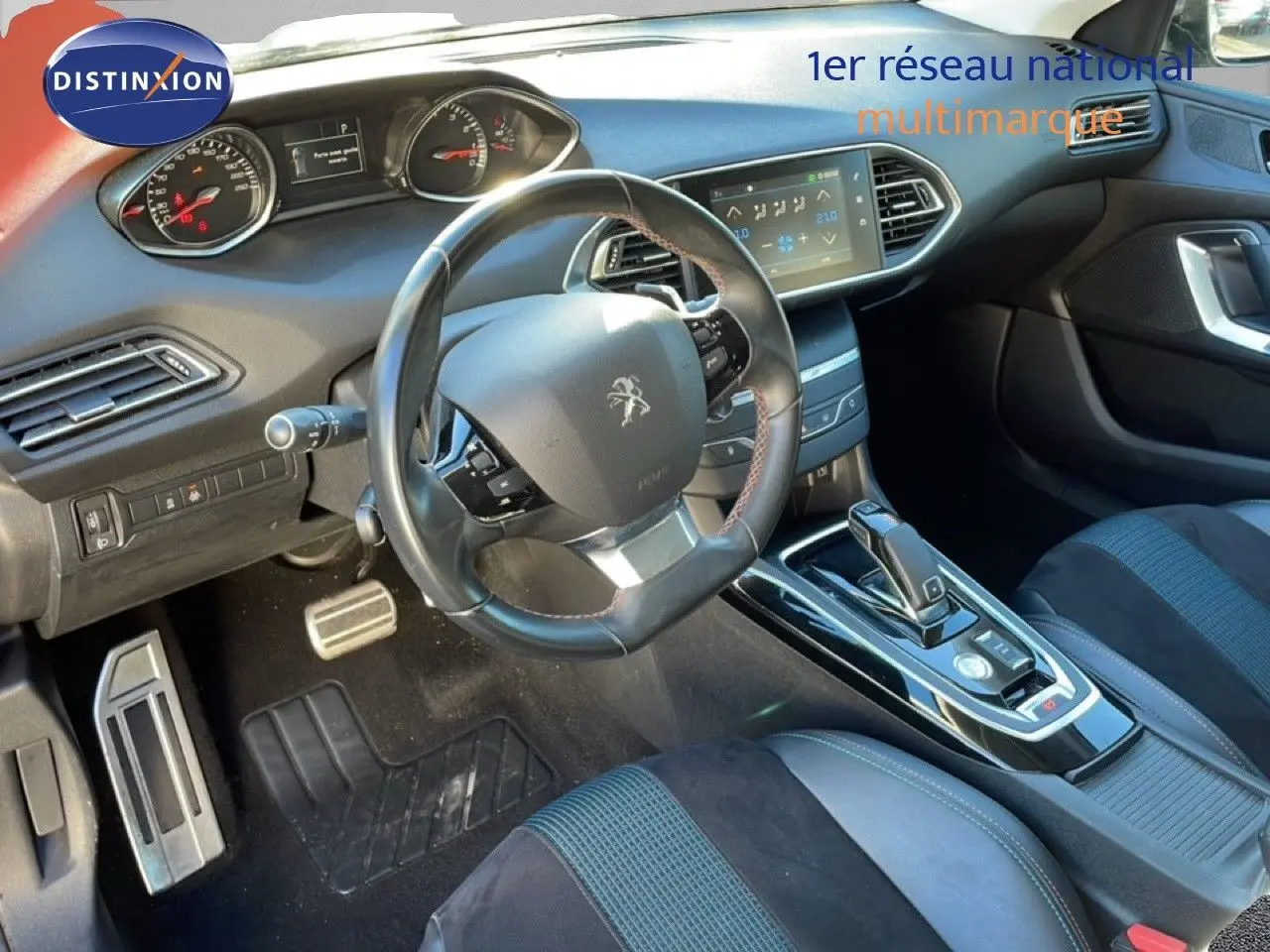 Vue intérieure côté conducteur de la Peugeot 308 gris Artense, avec volant cuir et écran tactile central visible.