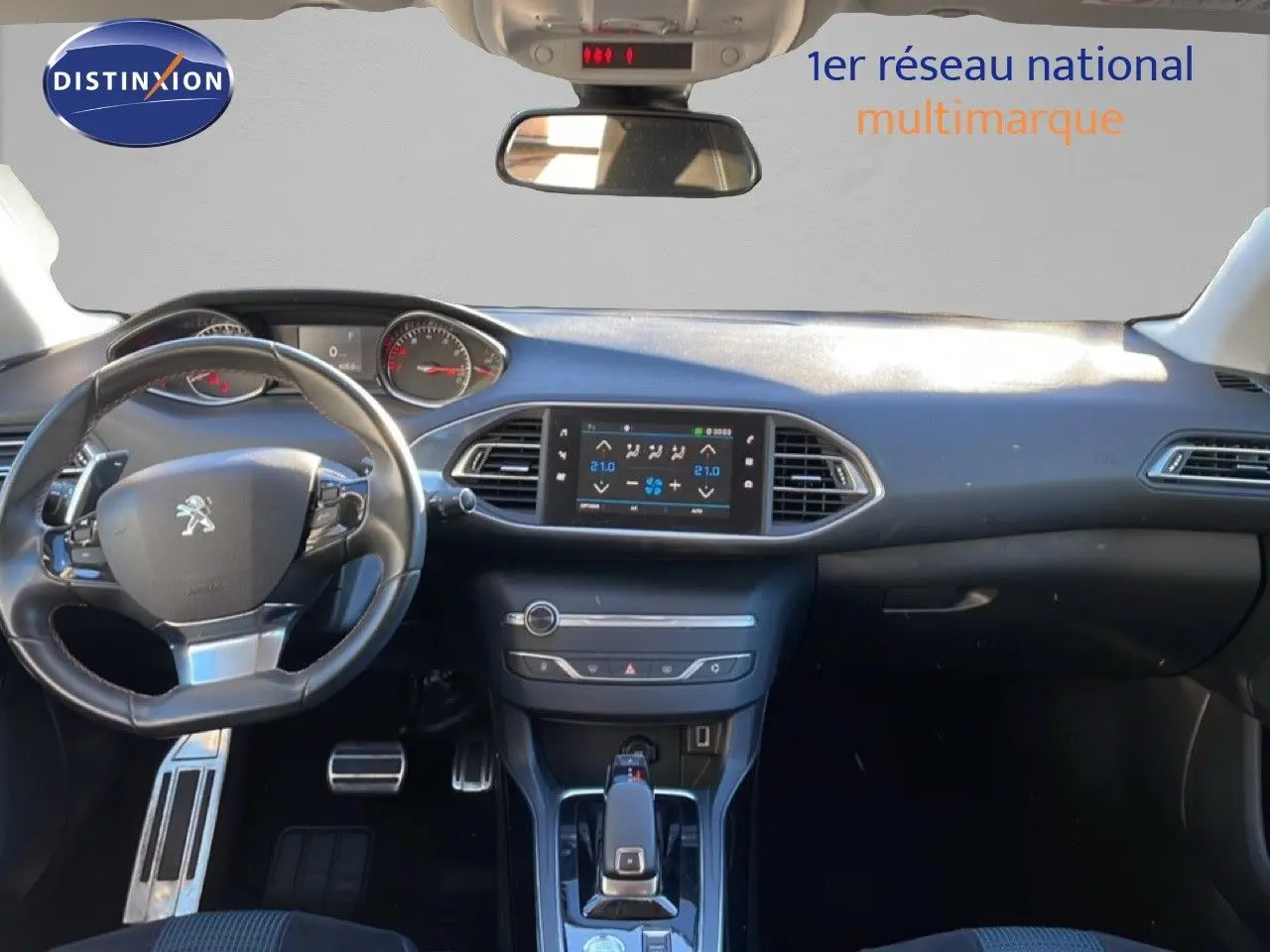 Vue intérieure avant du tableau de bord et volant noir de la Peugeot 308 gris Artense, avec écran tactile central allumé.