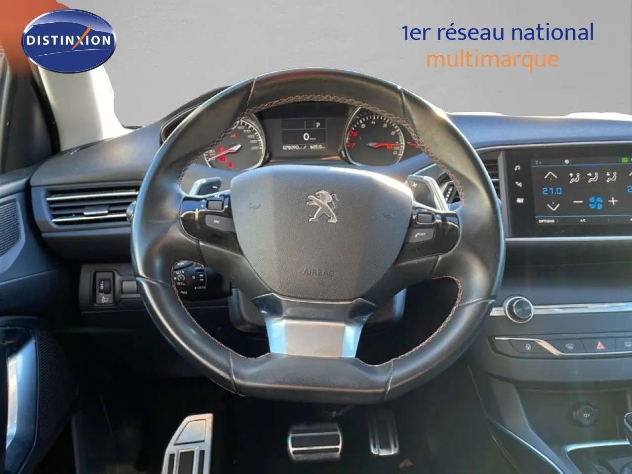 Vue intérieure centrée sur le volant cuir noir de la Peugeot 308 gris Artense, avec tableau de bord et écran tactile visibles.