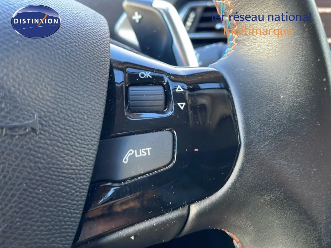 Gros plan sur les commandes au volant noir de la Peugeot 308 gris Artense, avec bouton "LIST" et molette "OK".