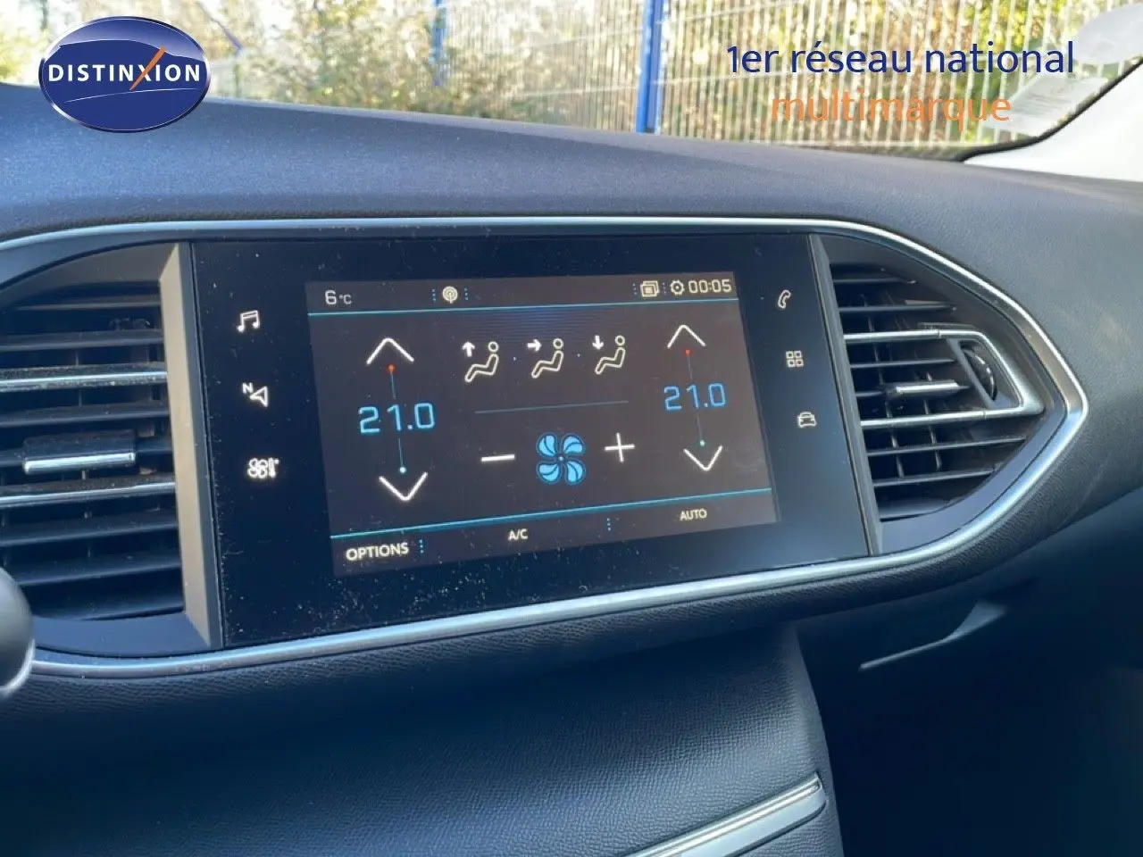 Écran tactile central du tableau de bord de la Peugeot 308 affichant la climatisation à 21°C, entouré de grilles d'aération noires.