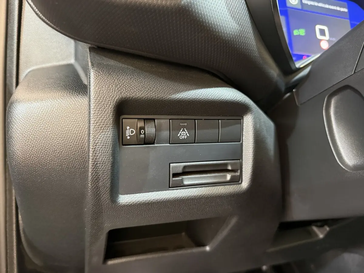 Gros plan sur les commandes de réglage des phares et d’aide à la conduite à gauche du volant dans un Citroën C5 Aircross gris clair 2023.