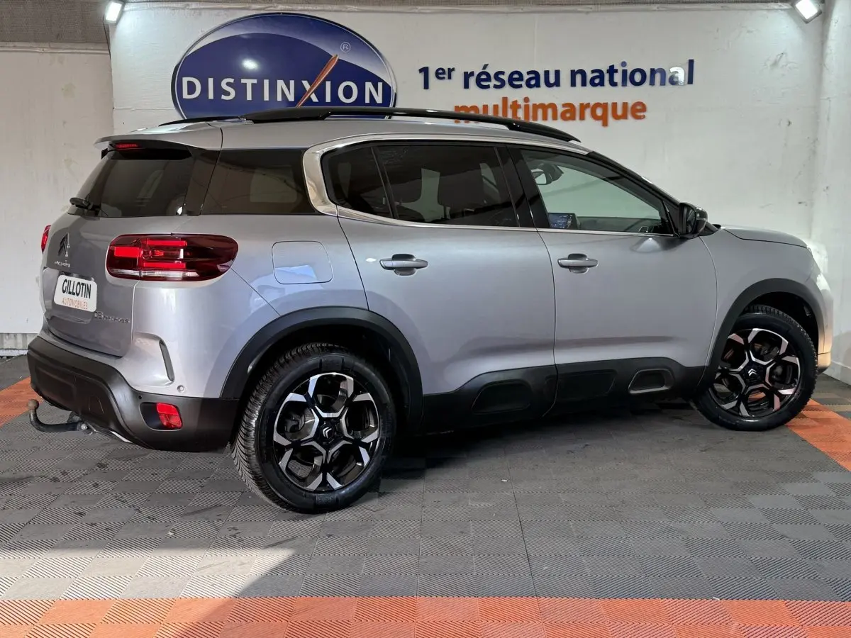 Vue latérale droite d'un Citroën C5 Aircross gris clair 2023, avec jantes noires et toit noir contrasté en intérieur showroom.