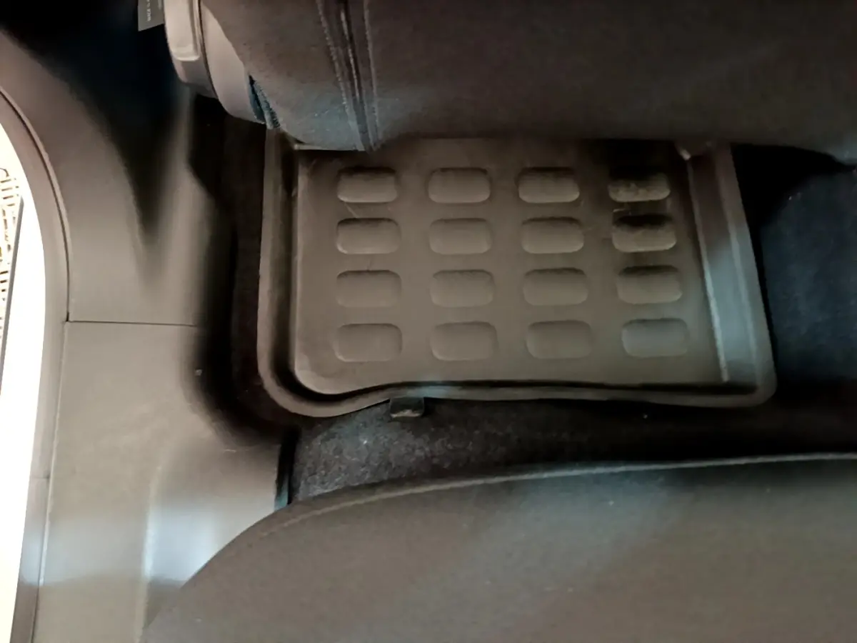 Vue rapprochée du tapis de sol arrière noir dans une Citroën C3 blanche, côté gauche, sous le siège passager.