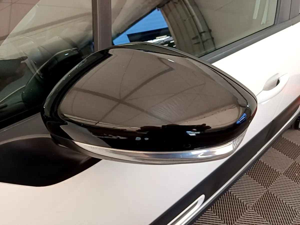 Gros plan sur le rétroviseur droit noir brillant d'une Citroën C3 blanche, avec poignée de porte visible en arrière-plan.
