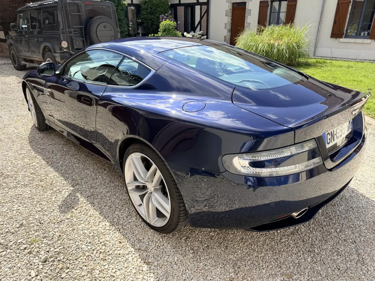 Vue 3/4 arrière droite d'une Aston Martin DB9 5.9 V12 bleu foncé brillant, avec jantes argentées et feux arrière LED.