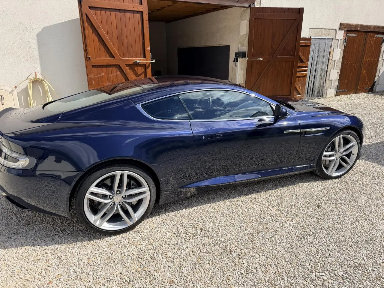 Vue latérale droite d'une Aston Martin DB9 bleu foncé 2016, soulignant ses jantes alliage et sa silhouette élégante.