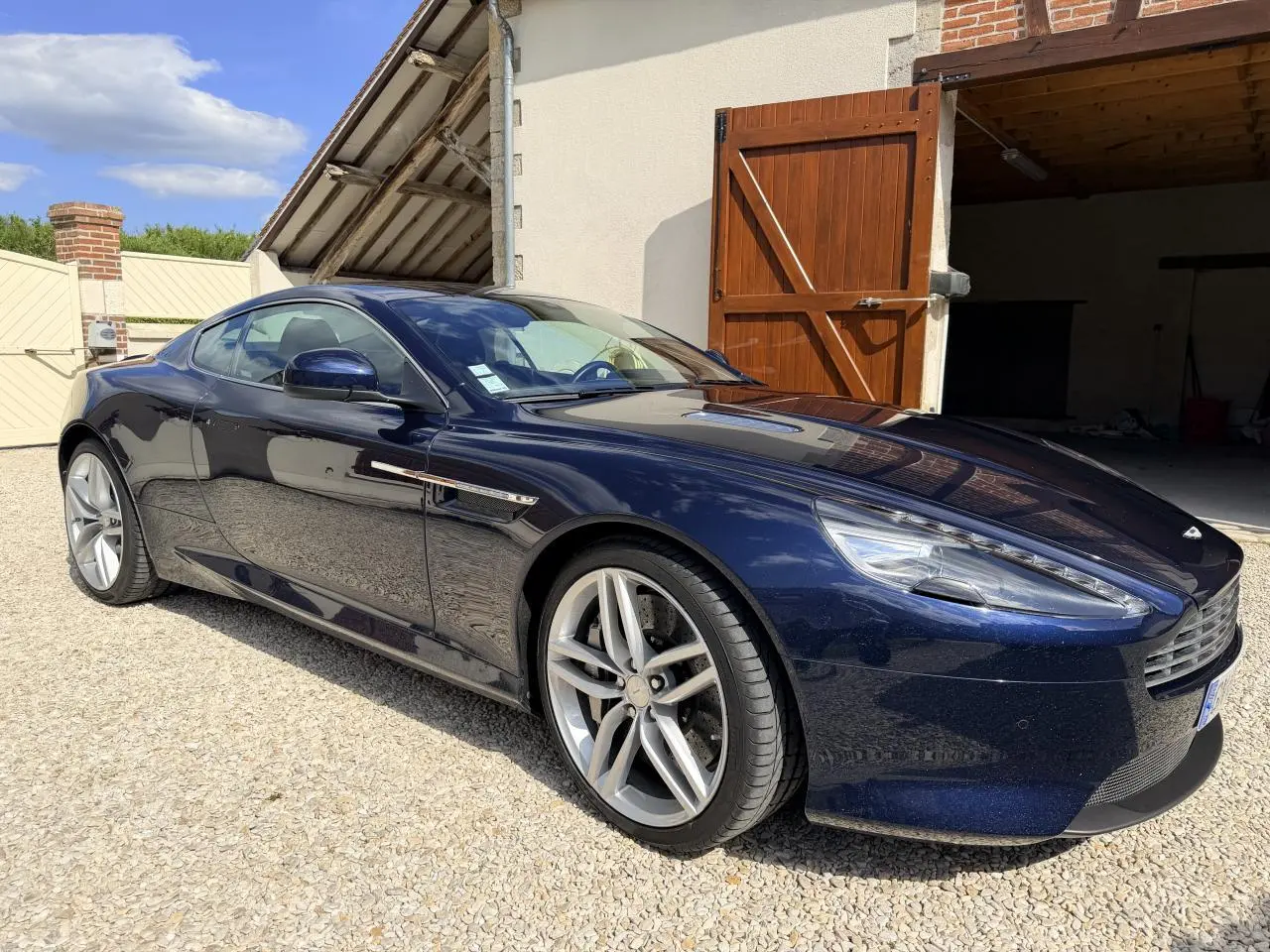 Aston Martin DB9 bleu foncé vue 3/4 avant droit, mettant en valeur ses jantes argentées et sa calandre distinctive.
