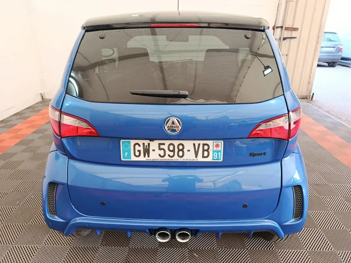 Vue arrière d'une Aixam Ambition 0.5 City Sport bleu 2024 avec double sortie d'échappement et logo Sport à droite.
