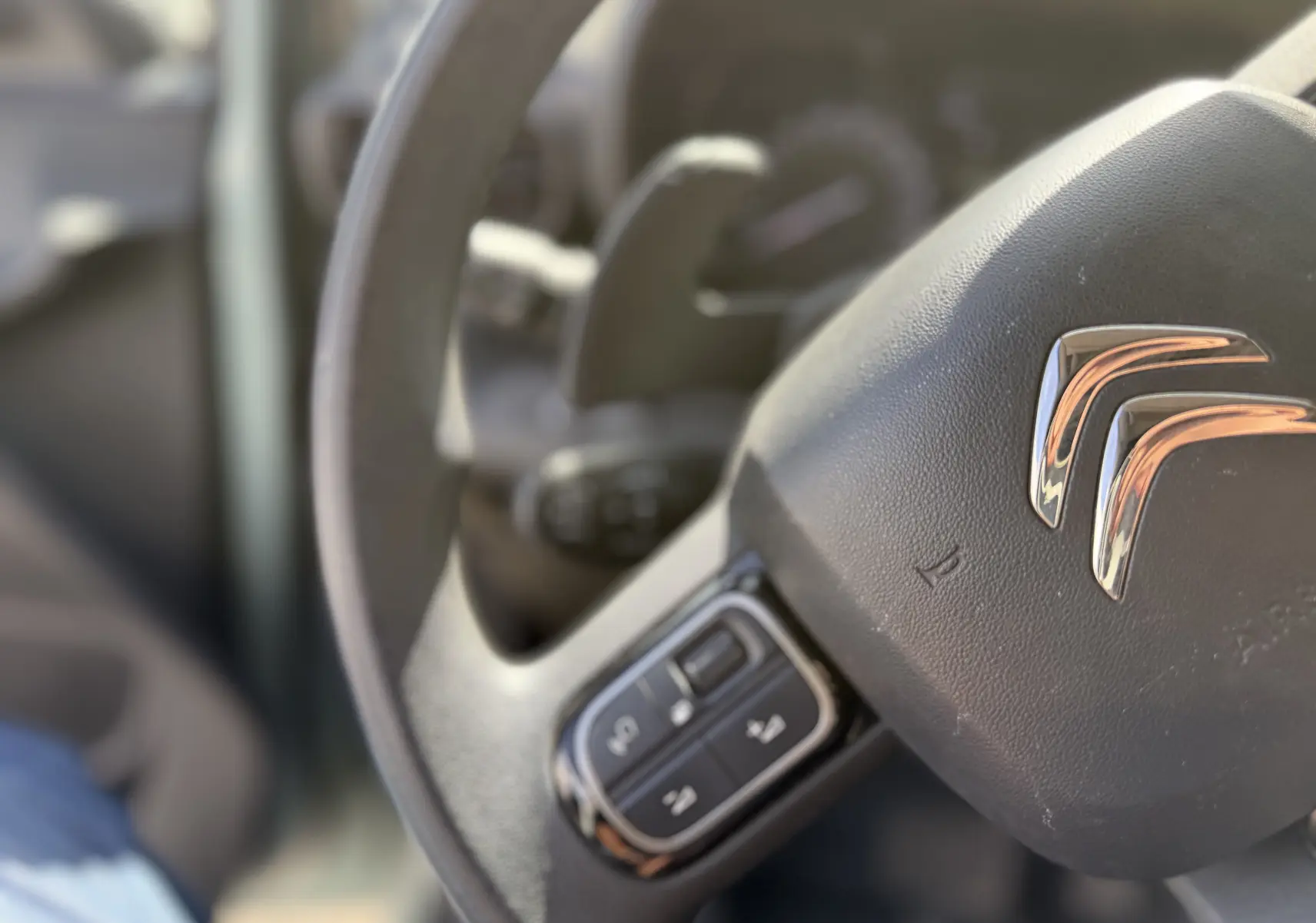 Gros plan sur le volant noir avec commandes intégrées du Citroën Berlingo FGN 2019, intérieur beige flouté en arrière-plan.