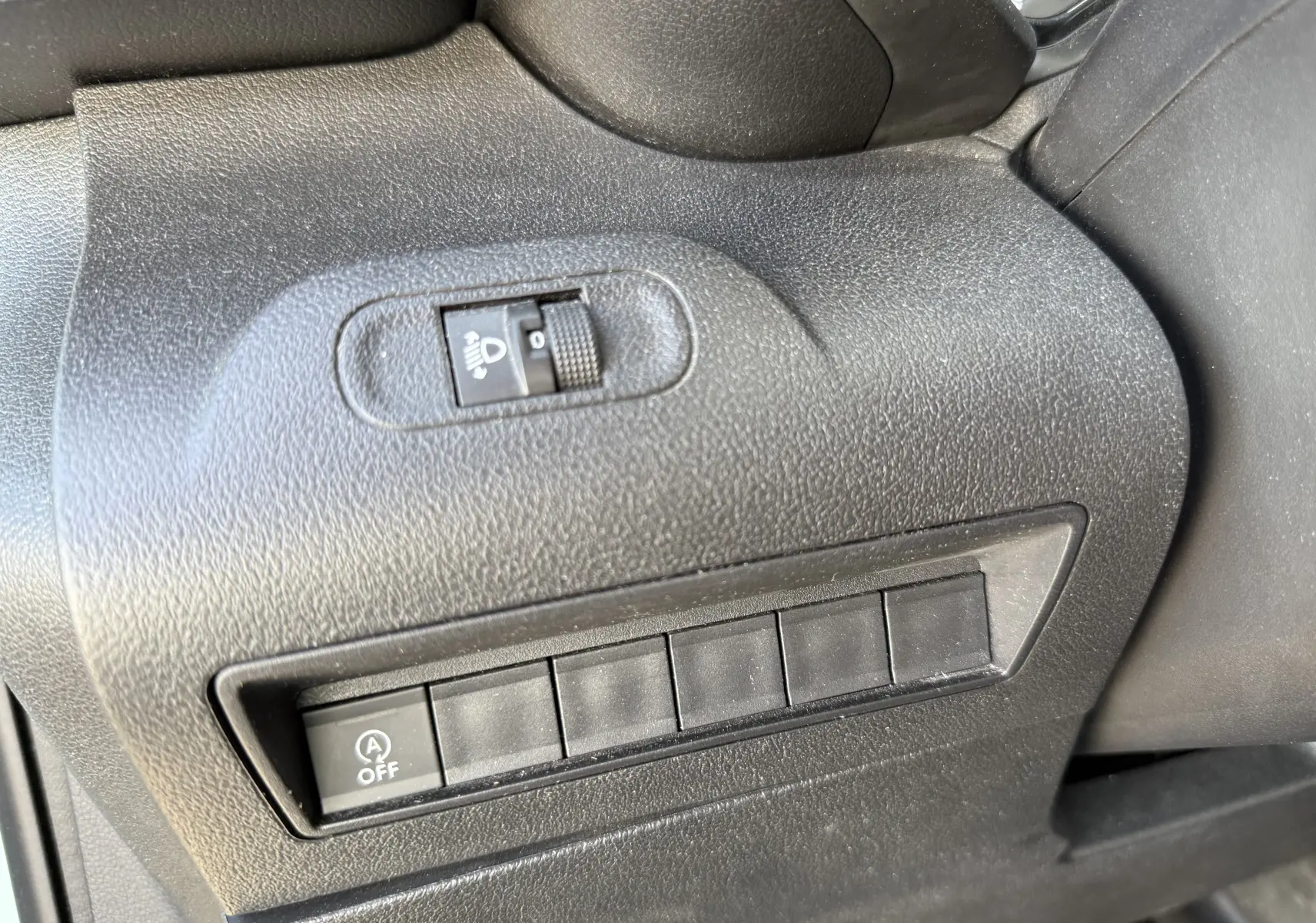 Gros plan sur les commandes noires côté gauche du tableau de bord du Citroën Berlingo beige, avec réglage des phares et bouton arrêt auto start-stop.